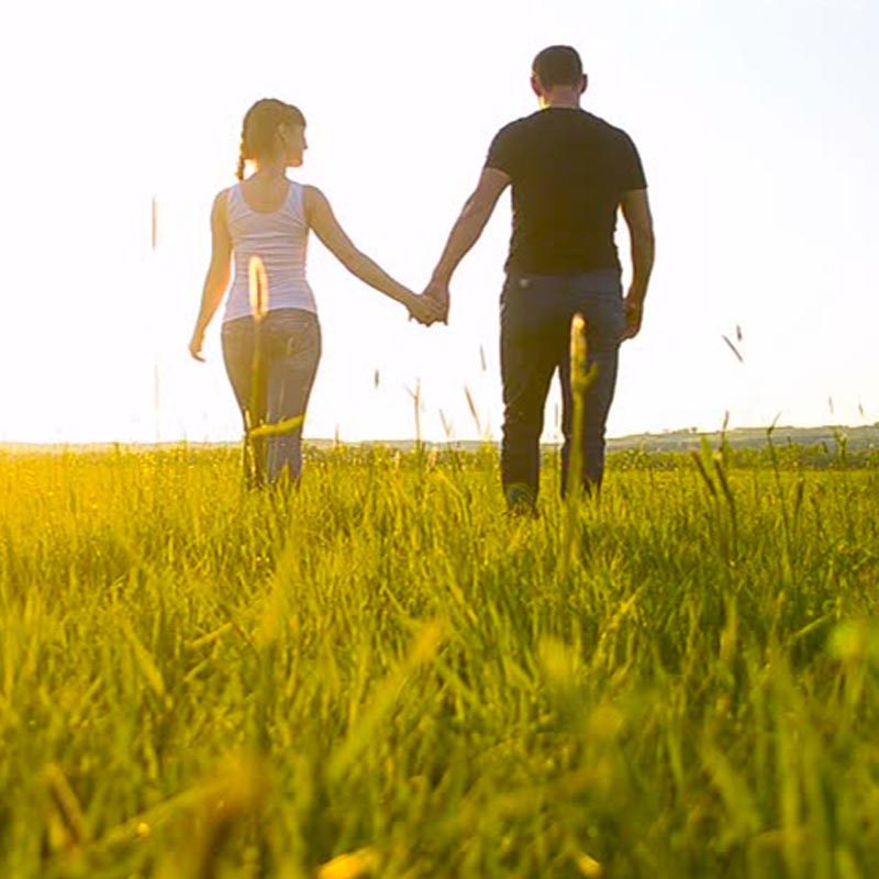 A man and woman holding hands while walking through the grass.