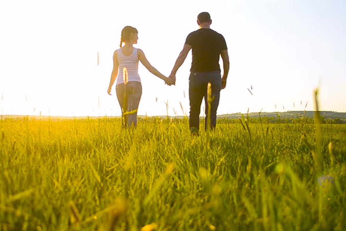 A man and woman holding hands while walking through the grass.